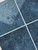 Marine blue peel and stick tiles installed behind a bathroom vanity with round mirror and modern fittings