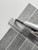 Person using a utility knife and metal ruler to easily cut a grey vinyl wall tile for custom fitting during a DIY project.