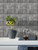 Kitchen countertop with white cabinets and a waterproof grey stone-effect tile backsplash behind a stovetop and plants
