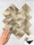 Hand applying a brass herringbone peel and stick tile sheet to a wall, demonstrating the easy DIY installation process.