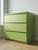 A modern three-drawer dresser completely resurfaced in Layed Matte Textured Matcha Green Vinyl Wrap MTMG25, situated on a light wood floor.