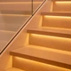 Warm UltraBright™ Accent Dynamic Tunable White IP20 LED Strip illuminating marble stair treads with a glass railing.
