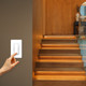 A hand tapping a Leona® Smart Dimmer Driver Switch on a wall to illuminate warm LED strips installed under wooden stairs.