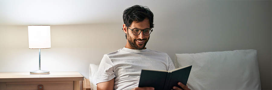 Person reading book on bed next to lamp