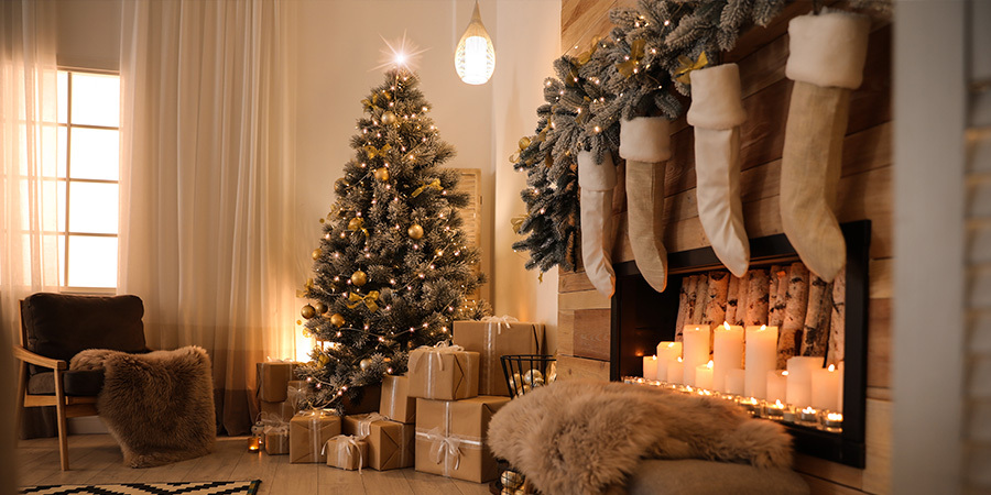Christmas tree lit with warm LED lights beside fireplace decorated with stockings and candles