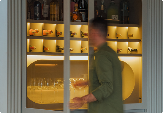 A man opening a wine cabinet with white LED linear lighting turning on automatically inside.