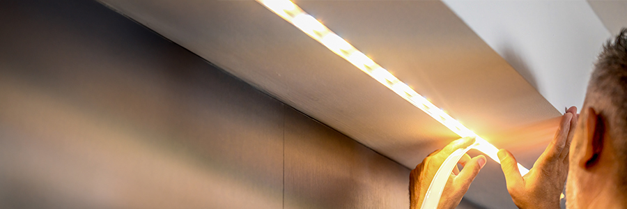 5 Reasons Your Kitchen LED Light Flickers (& How to Fix It) Person installing an LED strip light under a cabinet.