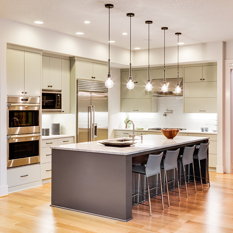 Modern kitchen with island, pendant LED lights, and stainless steel appliances.
