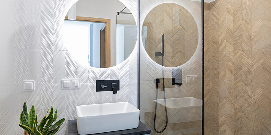 A modern bathroom with a round mirror illuminated with bright white LED lighting