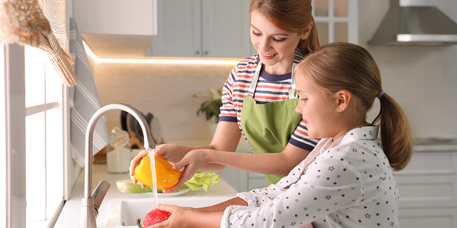 Family washing food under LED kitchen cabinet lighting