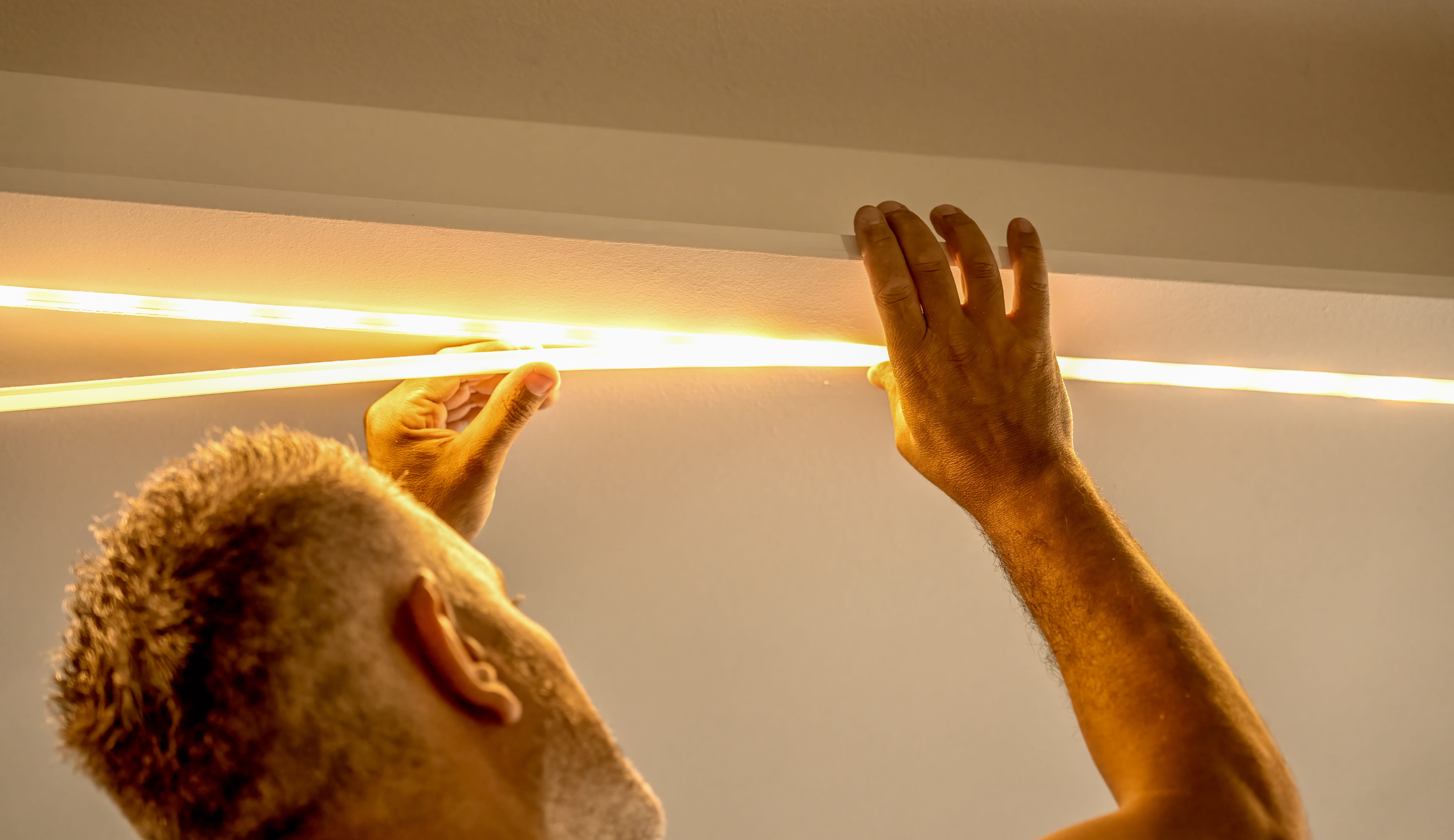 A man opening a wine cabinet with white LED linear lighting turning on automatically inside.