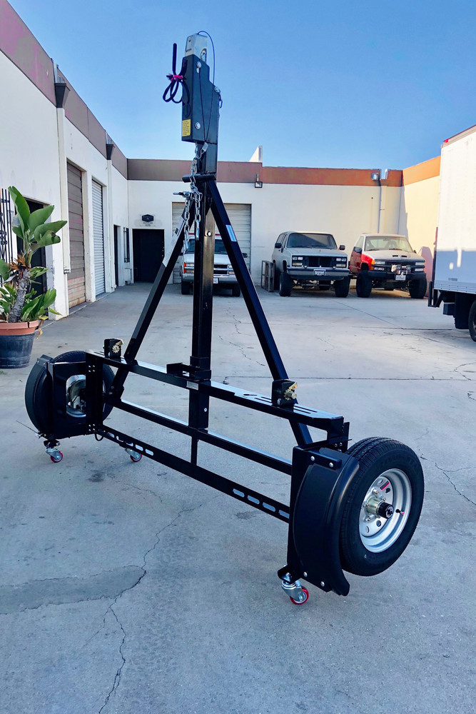 A black motorcycle trailer standing vertically on a concrete driveway, supported by the red EZ-Haul Casters. The kit allows the trailer to be stored upright to save space in a garage or driveway."