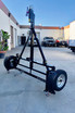 A black motorcycle trailer standing vertically on a concrete driveway, supported by the red EZ-Haul Casters. The kit allows the trailer to be stored upright to save space in a garage or driveway."