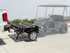 The Compact Caddy folding golf cart and utility trailer hitched to a white pickup truck with a golf cart parked nearby
