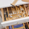 A top-down view of a bamboo bag organizer placed inside a kitchen drawer, with its four compartments neatly filled with gallon, quart, sandwich, and snack-sized plastic storage bags.