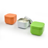 The three colorful candle tins are shown on a clean white surface; the orange tin is open, the white tin is closed, and the lime green tin is partially visible, giving a sense of the complete set.