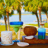 The Volcano candle is displayed in a vibrant, tropical outdoor setting alongside other summer-themed candles and a coconut, evoking a vacation atmosphere.