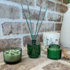 The green glass home fragrance trio is displayed in a bright, modern living room setting, adding a touch of sophisticated decor to the space.
