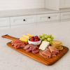Charcuterie board on a bright kitchen island, filled with assorted meats, cheeses, grapes, raspberries, and crackers, with modern white cabinetry in the background.
