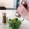 Hand using the acacia pepper grinder to season vegetables in a bowl.