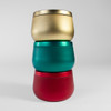 Stacked trio of holiday wood-wick candle tins—gold, teal, and red—on a snowy surface