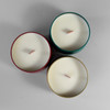 Top view of two holiday candle tins with lids and exposed wood wicks arranged on faux snow