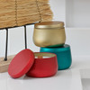 Holiday wood-wick candle tins with matching gold, teal, and red lids styled on faux snow