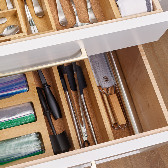 The adjustable bamboo dividers are shown organizing a cluttered office or junk drawer, neatly separating pens, scissors, and other miscellaneous items into tidy compartments.