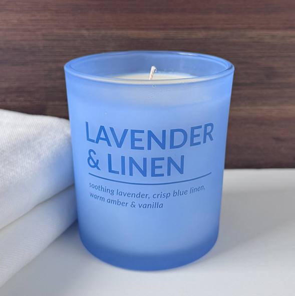 A Lavender & Linen scented soy candle in a tranquil, frosted light blue glass jar is displayed next to a soft, folded white towel, evoking a sense of calm and relaxation. A Lavender & Linen scented soy candle in a tranquil, frosted light blue glass jar is displayed next to a soft, folded white towel, evoking a sense of calm and relaxation.