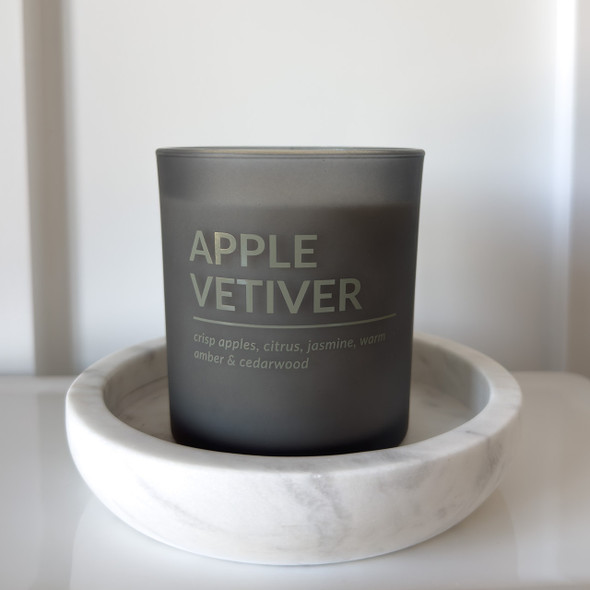 The matte black candle jar is shown resting on a round, white decorative coaster, demonstrating a stylish way to display it and protect surfaces.