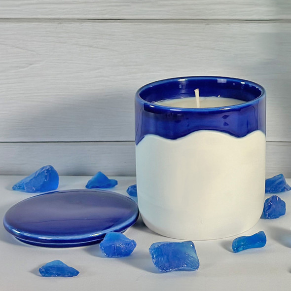 A Summer Days scented soy candle in a beautiful, artisan blue and white ceramic canister is displayed with its lid off, surrounded by decorative blue sea glass to evoke a fresh, coastal feeling. A Summer Days scented soy candle in a beautiful, artisan blue and white ceramic canister is displayed with its lid off, surrounded by decorative blue sea glass to evoke a fresh, coastal feeling.