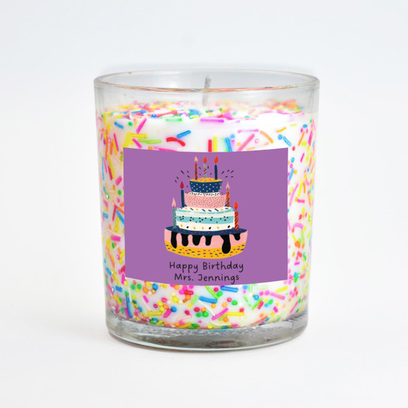 A festive Cake Sprinkles Inclusion Candle in a clear glass jar, featuring a personalized purple label with a birthday cake illustration and the text "Happy Birthday Mrs. Jennings." A festive Cake Sprinkles Inclusion Candle in a clear glass jar, featuring a personalized purple label with a birthday cake illustration and the text "Happy Birthday Mrs. Jennings."