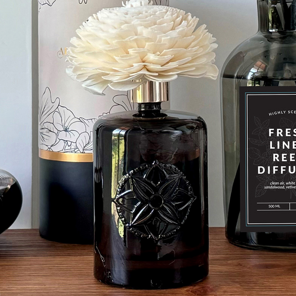 A decorative Flower Reed Diffuser, featuring an embossed dark glass bottle and a beautiful white sola paper flower, is displayed on a shelf as an elegant piece of home decor. A decorative Flower Reed Diffuser, featuring an embossed dark glass bottle and a beautiful white sola paper flower, is displayed on a shelf as an elegant piece of home decor.