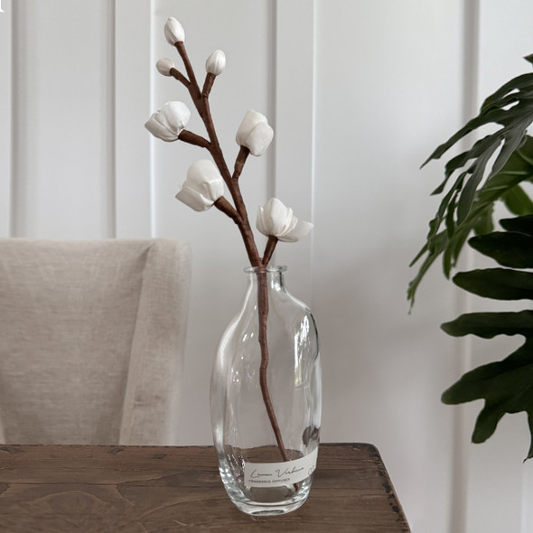 A Lemon Verbena flower reed diffuser, featuring a clear glass bottle and a beautiful, hand-made sola paper flower reed shaped like a budding branch, is displayed as an elegant centerpiece on a wooden table. A Lemon Verbena flower reed diffuser, featuring a clear glass bottle and a beautiful, hand-made sola paper flower reed shaped like a budding branch, is displayed as an elegant centerpiece on a wooden table.