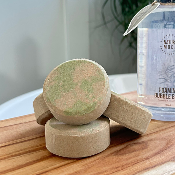 The shower steamers are shown in a bathroom setting on a small wooden board next to a bottle of soap, suggesting a relaxing, therapeutic shower experience. The shower steamers are shown in a bathroom setting on a small wooden board next to a bottle of soap, suggesting a relaxing, therapeutic shower experience.