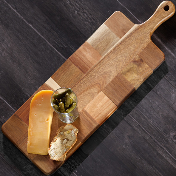 An Acacia Mosaic Paddle Board featuring a mosaic pattern of wood pieces, displayed with cheese, crackers, and pickles on a dark wooden surface. The board has an extended handle. An Acacia Mosaic Paddle Board featuring a mosaic pattern of wood pieces, displayed with cheese, crackers, and pickles on a dark wooden surface. The board has an extended handle.