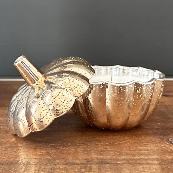 Gold mercury glass pumpkin candle with the lid propped open on a wooden table. Gold mercury glass pumpkin candle with the lid propped open on a wooden table.