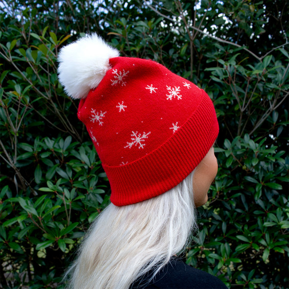 Outdoor close-up of red snowflake beanie with white faux-fur pom-pom Outdoor close-up of red snowflake beanie with white faux-fur pom-pom