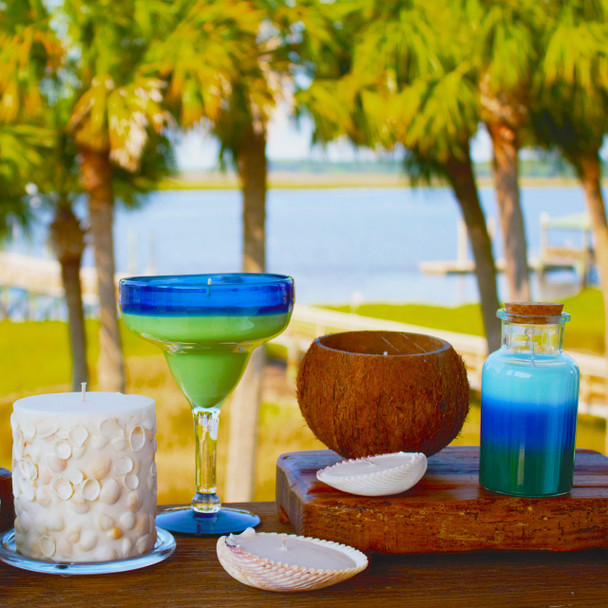 The Volcano candle is displayed in a vibrant, tropical outdoor setting alongside other summer-themed candles and a coconut, evoking a vacation atmosphere.