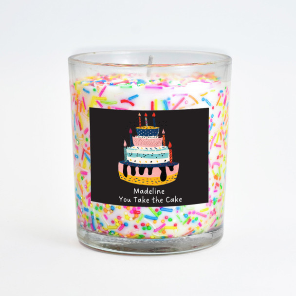 The sprinkles inclusion candle is displayed with an alternate personalized label design, featuring a black background and a cupcake illustration with the text "Madeline You Take the Cake."