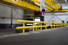 Long yellow steel guardrail system installed inside a large industrial warehouse, providing heavy-duty impact protection along equipment and traffic lane