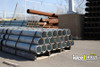 Bundle of galvanized steel pipes stacked on a wooden pallet at an industrial yard with additional pipe stock in the background