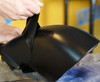 A person peels a layer of black, rubberized coating off a smooth, curved surface to demonstrate the product's removable nature.