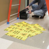 Worker placing yellow ‘Caution’ floor mats around a wet floor area beside a ladder and open toolbox