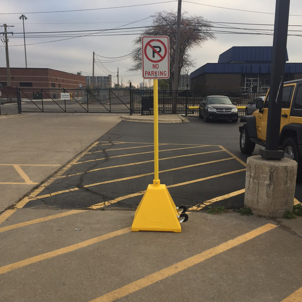 Yellow pyramid portable sign base with vertical post and no parking sign installed in a parking lot, designed for temporary traffic or parking guidance