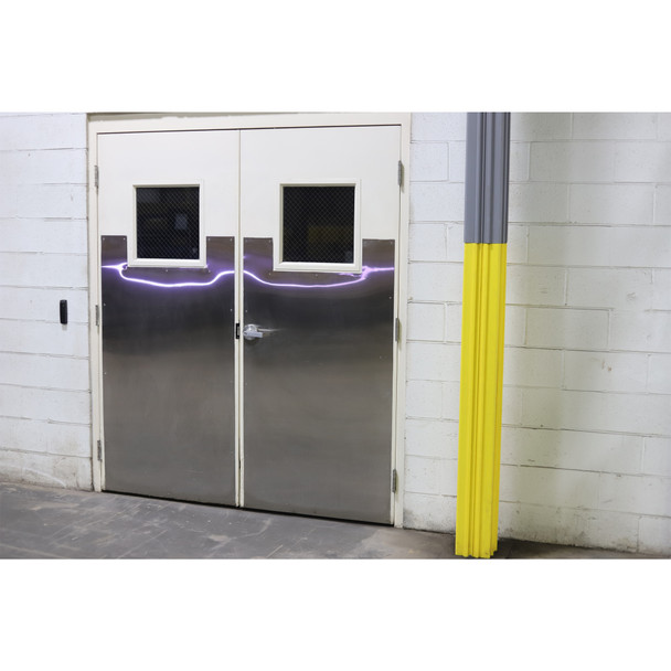 Grey and yellow column guard installed on a structural pillar next to double metal-clad industrial doors.