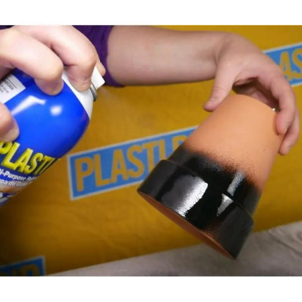A person applies a black rubberized spray coating to the base of a terracotta flower pot.