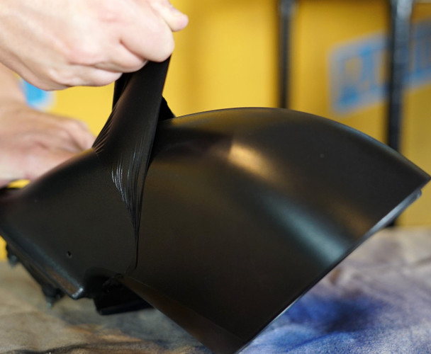 A person peels a layer of black, rubberized coating off a smooth, curved surface to demonstrate the product's removable nature.