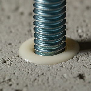 Close-up of metal anchor bolt embedded in concrete with smooth gray sealant applied around the base to seal and protect the penetration.