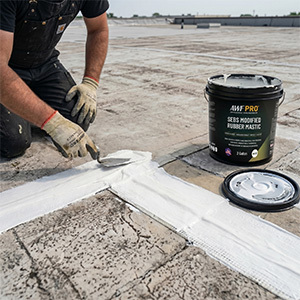 Contractor applying white rubber roof mastic with reinforcing fabric on flat commercial roof beside open two gallon coating pail